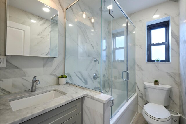 full bath featuring tile walls, vanity, toilet, and bath / shower combo with glass door