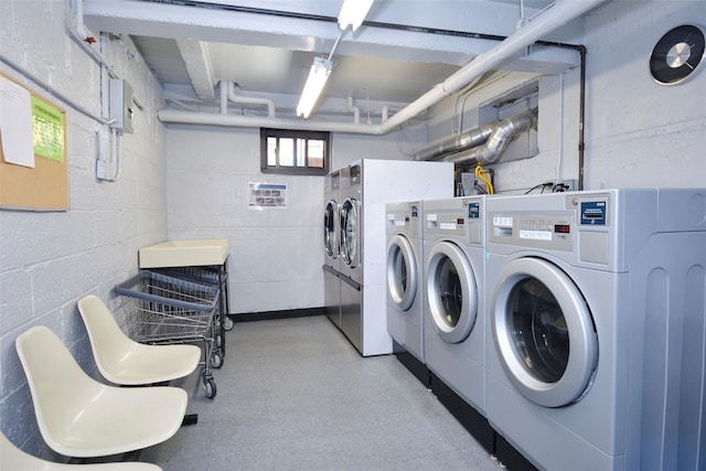 shared laundry area with concrete block wall, light floors, and separate washer and dryer