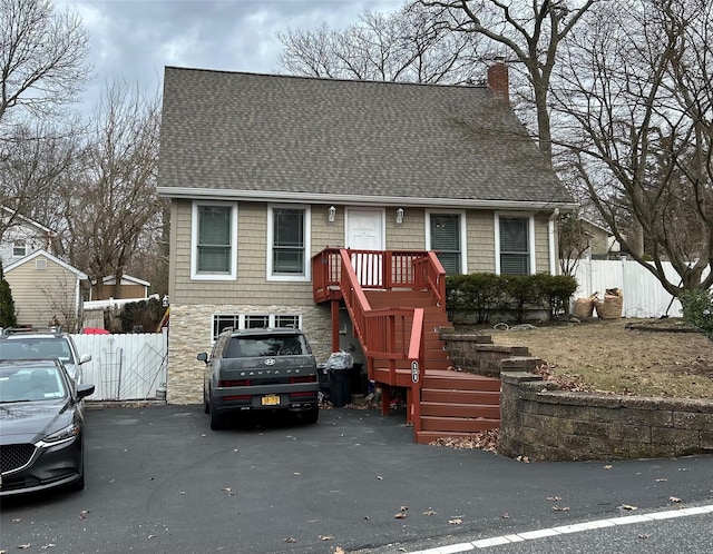 view of front of house featuring a shingled roof, fence, stone siding, and a chimney