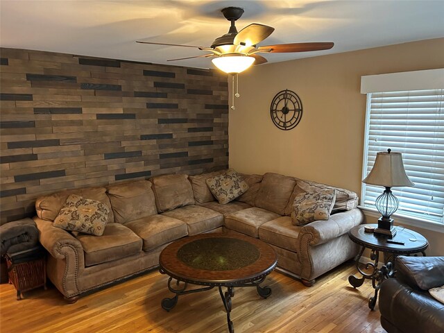 living area featuring light wood finished floors, ceiling fan, and an accent wall