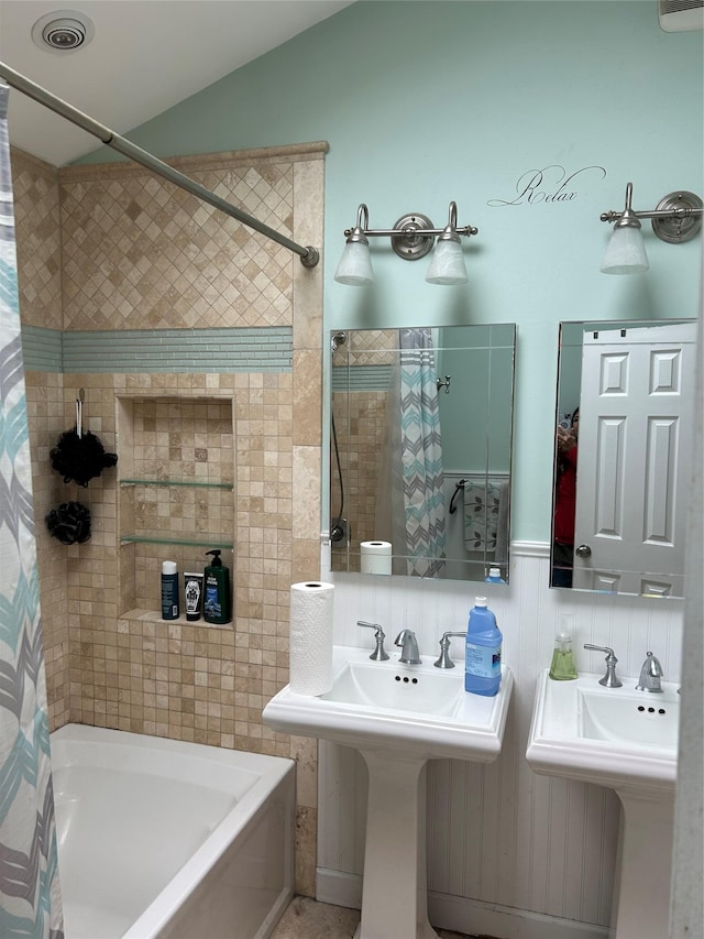 bathroom featuring vaulted ceiling, shower / bathtub combination with curtain, and a sink