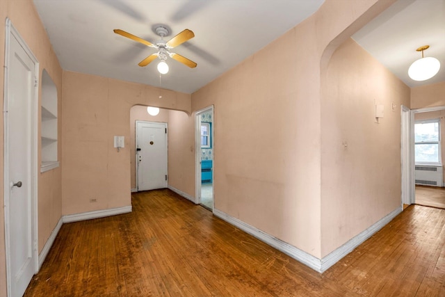 entrance foyer featuring arched walkways, radiator heating unit, ceiling fan, and wood-type flooring