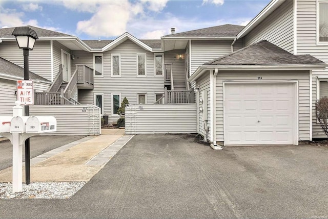 view of property with a garage, aphalt driveway, roof with shingles, and stairs