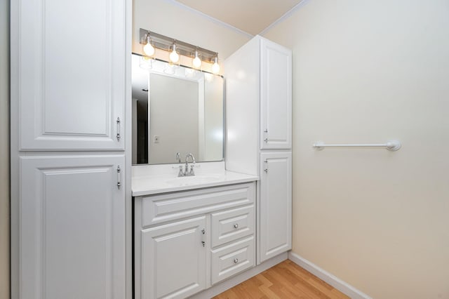 bathroom featuring baseboards, wood finished floors, vanity, and crown molding