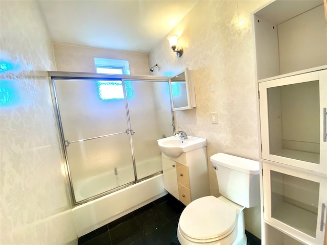 bathroom featuring toilet, shower / bath combination with glass door, tile patterned floors, vanity, and tile walls