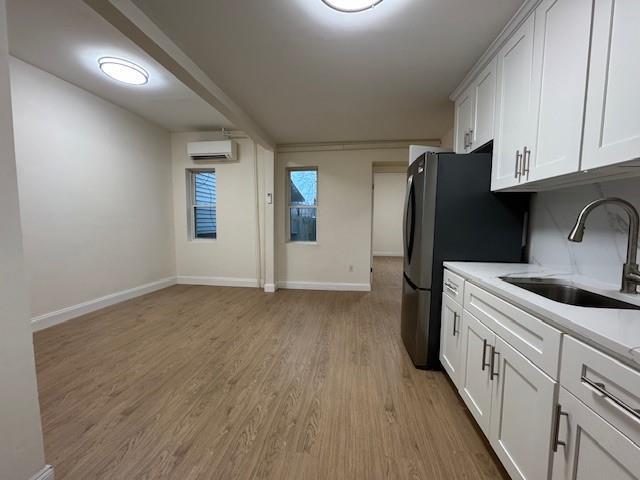 kitchen featuring light countertops, a wall mounted AC, light wood-style floors, white cabinets, and a sink