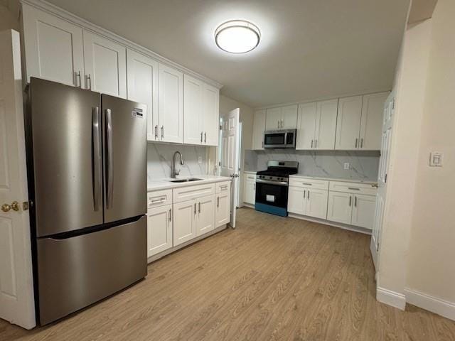 kitchen with white cabinets, appliances with stainless steel finishes, light countertops, light wood-type flooring, and a sink