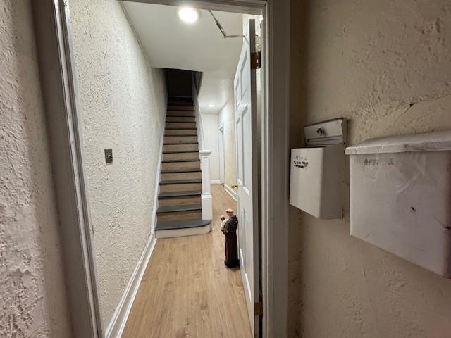 hallway with a textured wall, light wood finished floors, and stairway