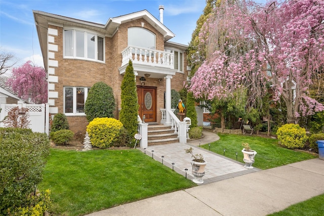 view of front of property featuring a balcony, a front yard, fence, and brick siding