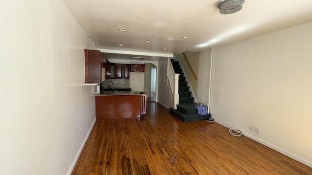 unfurnished living room with dark wood-type flooring, a sink, arched walkways, and stairway