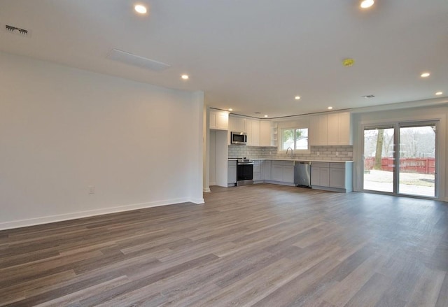 unfurnished living room with recessed lighting, a sink, wood finished floors, visible vents, and baseboards