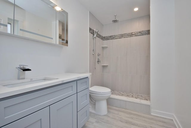 bathroom with toilet, wood finished floors, vanity, baseboards, and a tile shower