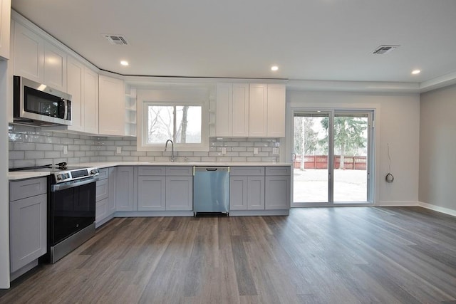 kitchen with appliances with stainless steel finishes, decorative backsplash, a sink, and wood finished floors