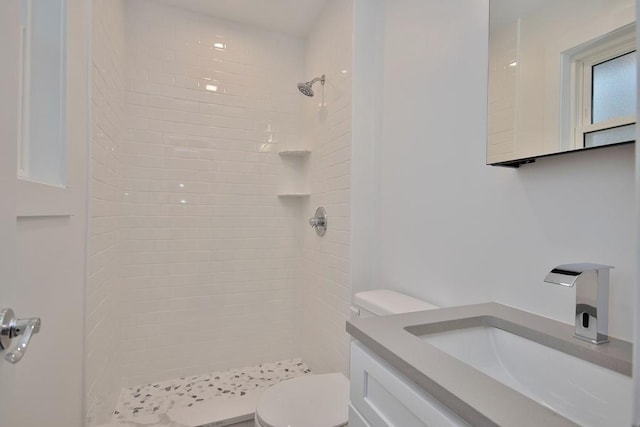 bathroom with tiled shower, vanity, and toilet