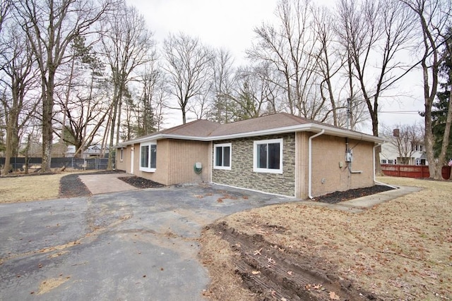 exterior space with stone siding, a patio area, fence, and aphalt driveway