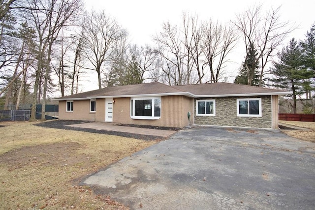 ranch-style home with driveway, stone siding, and fence