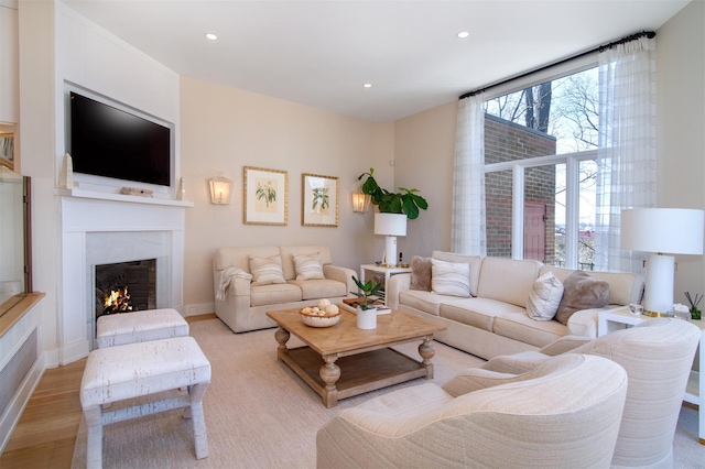 living area with light wood finished floors, recessed lighting, baseboards, and a lit fireplace