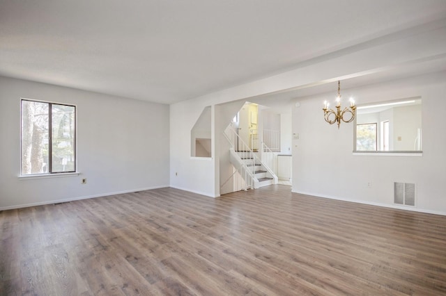 unfurnished living room with a wealth of natural light, visible vents, wood finished floors, and stairway