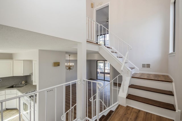 stairway with wood finished floors, visible vents, a high ceiling, a textured ceiling, and ceiling fan with notable chandelier