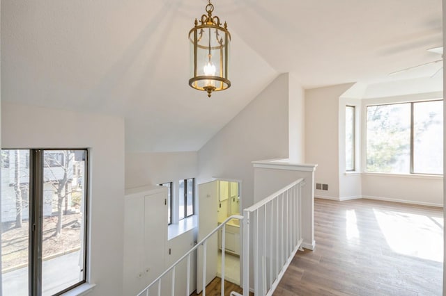 hall featuring visible vents, baseboards, vaulted ceiling, an upstairs landing, and wood finished floors