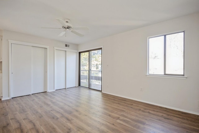 unfurnished bedroom featuring access to exterior, baseboards, multiple closets, and wood finished floors