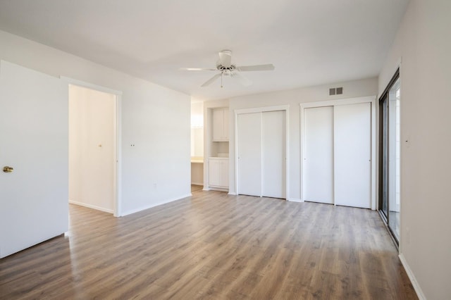 unfurnished bedroom with visible vents, multiple closets, wood finished floors, baseboards, and ceiling fan