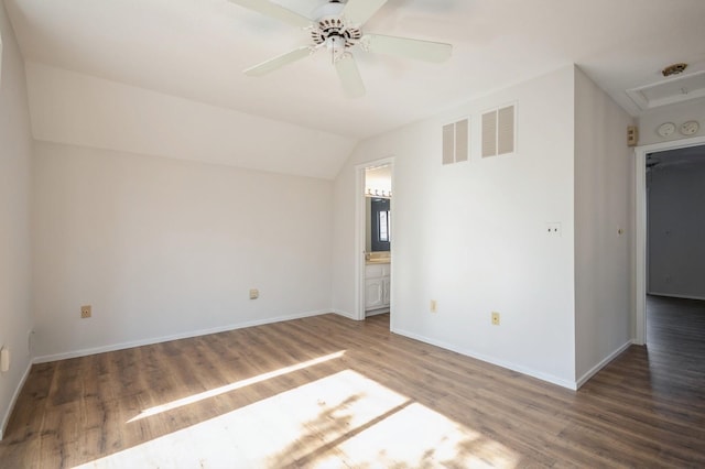 empty room with vaulted ceiling, wood finished floors, visible vents, and baseboards