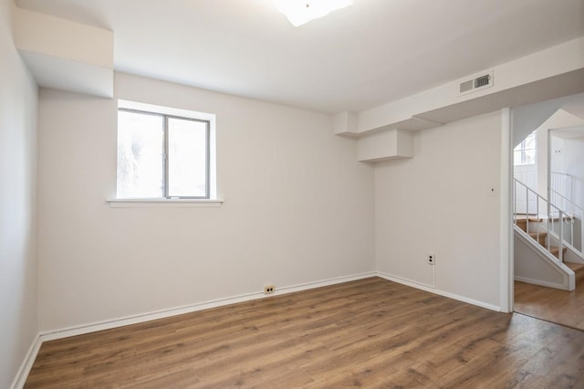 unfurnished room with stairway, wood finished floors, visible vents, and baseboards