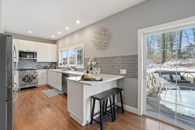 kitchen featuring light wood finished floors, a peninsula, a sink, appliances with stainless steel finishes, and white cabinetry