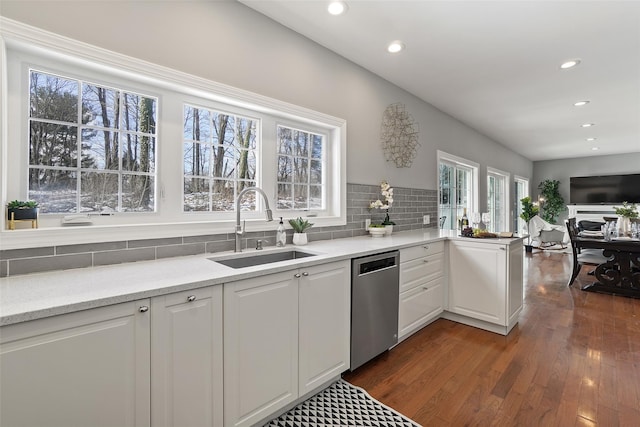 kitchen with dark wood-type flooring, a sink, backsplash, stainless steel dishwasher, and white cabinetry