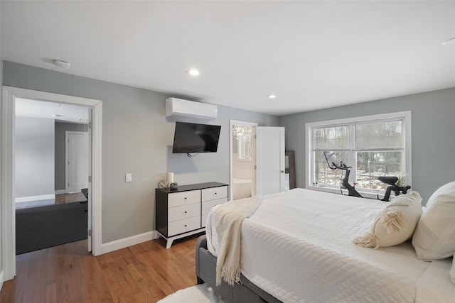 bedroom with baseboards, a wall mounted air conditioner, recessed lighting, light wood-style floors, and ensuite bath