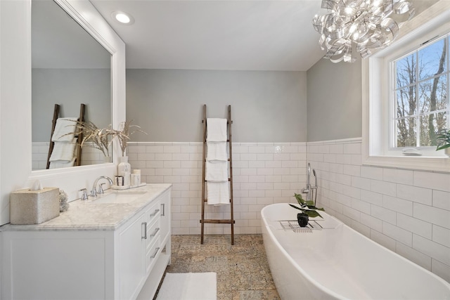 full bathroom with vanity, recessed lighting, a freestanding bath, wainscoting, and tile walls