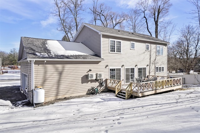 snow covered back of property featuring fence, a deck, and roof with shingles