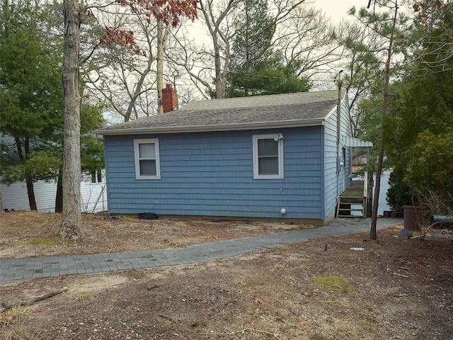 view of property exterior featuring driveway, a shingled roof, a chimney, and fence