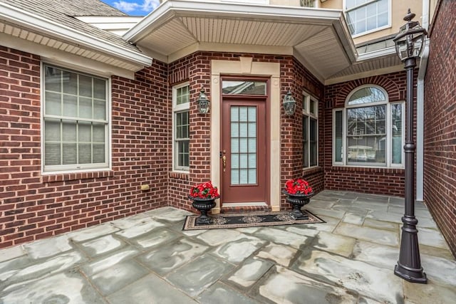 property entrance with a shingled roof and brick siding