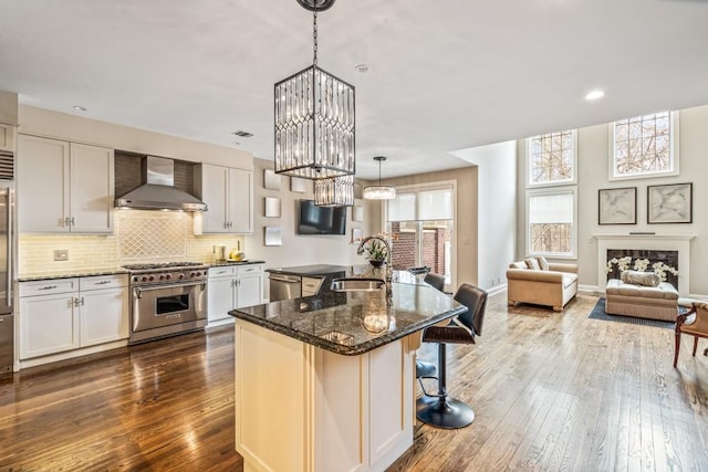 kitchen with stainless steel appliances, wall chimney range hood, dark wood-style flooring, and a sink