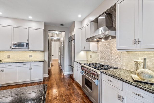 kitchen featuring dark wood-style floors, backsplash, wall chimney range hood, dark stone countertops, and high quality appliances