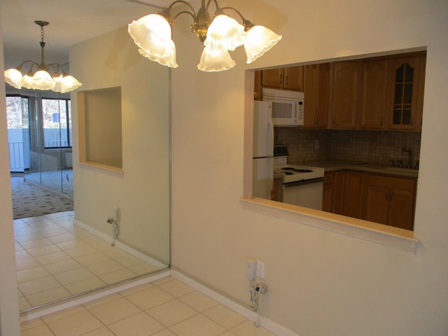 kitchen with white appliances, light tile patterned floors, decorative backsplash, brown cabinets, and an inviting chandelier