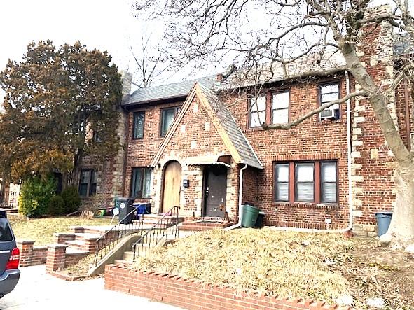 tudor-style house featuring cooling unit and brick siding