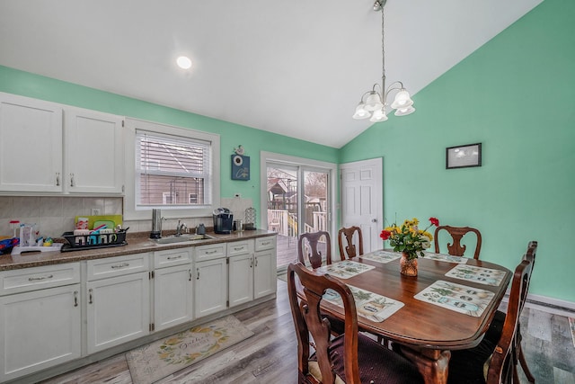 dining room featuring a notable chandelier, vaulted ceiling, and light wood-style flooring