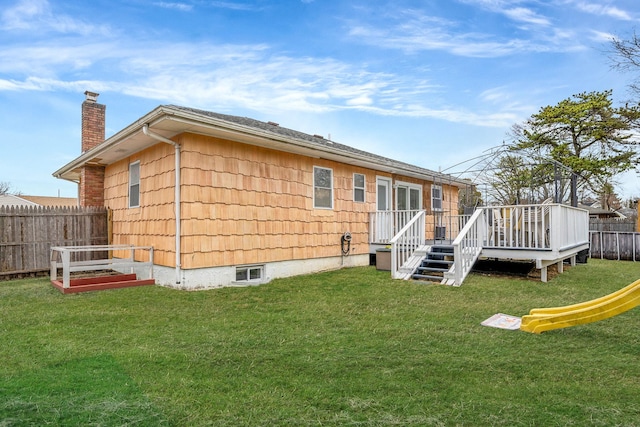 rear view of house featuring a deck, a yard, a chimney, and fence