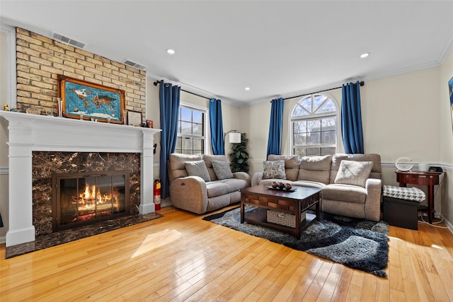 living room featuring hardwood / wood-style flooring, a fireplace, visible vents, and crown molding