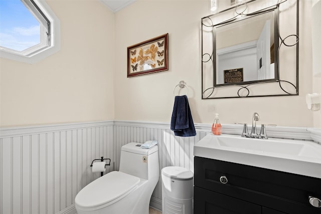 half bathroom with toilet, a wainscoted wall, and vanity