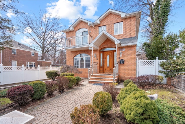 view of front of house featuring fence private yard, a gate, brick siding, and a balcony