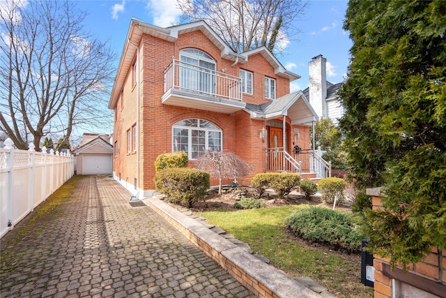 view of front facade with a balcony, a garage, brick siding, an outdoor structure, and fence