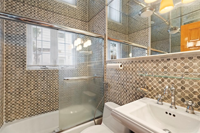 full bath featuring toilet, enclosed tub / shower combo, tile walls, and a sink