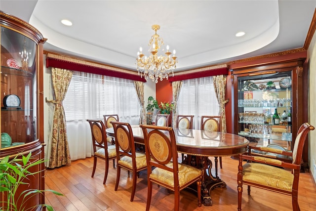 dining space with light wood finished floors, a raised ceiling, and a notable chandelier