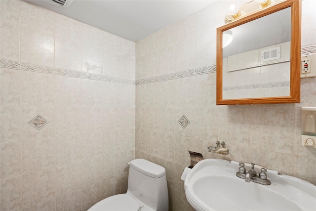 bathroom with toilet, tile walls, visible vents, and a sink