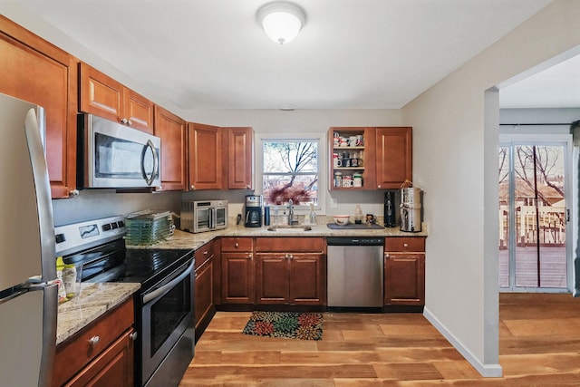 kitchen with light stone counters, light wood finished floors, appliances with stainless steel finishes, a sink, and baseboards