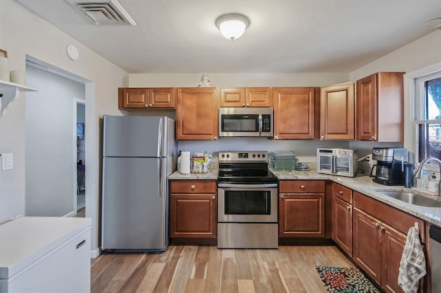 kitchen with a sink, visible vents, light wood-style floors, appliances with stainless steel finishes, and brown cabinetry